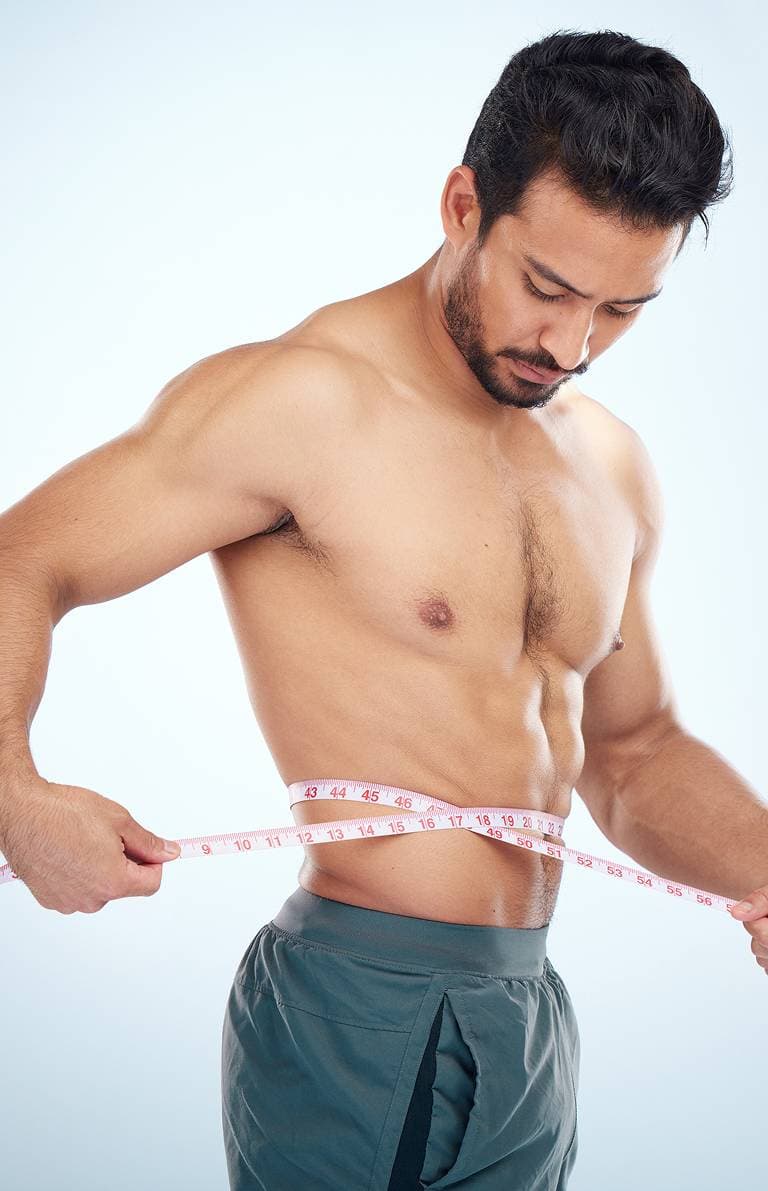 A man measuring his waist with a tape measure after a body composition scan